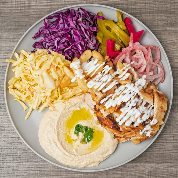 A SK Shawarma plate with chicken, hummus, fries, pickled vegetables, and red and white cabbage.