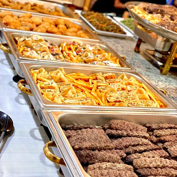 A buffet spread of Middle Eastern dishes, including shawarma wraps, fries, and kofta in chafing dishes.