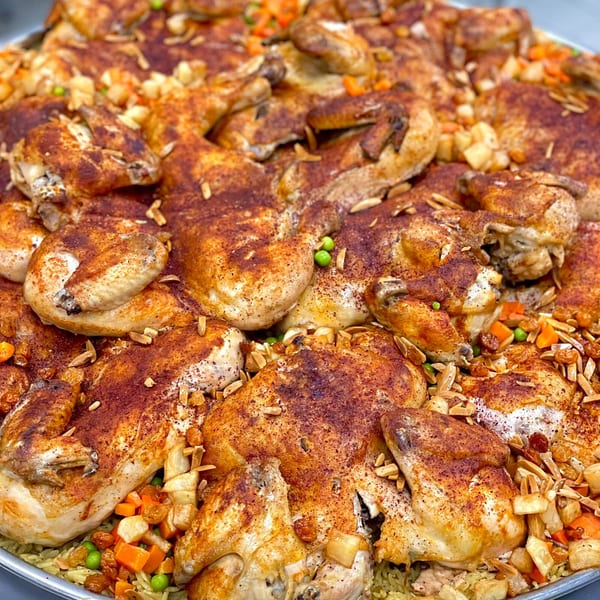 A large platter of roasted chicken pieces, seasoned with spices, almonds, and vegetables.