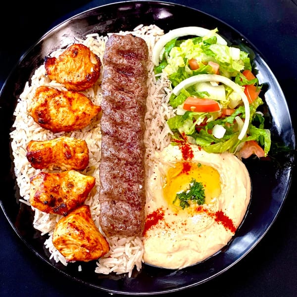 SK Shawarma's chicken and beef kebab plate with rice, salad, and hummus on a black plate.