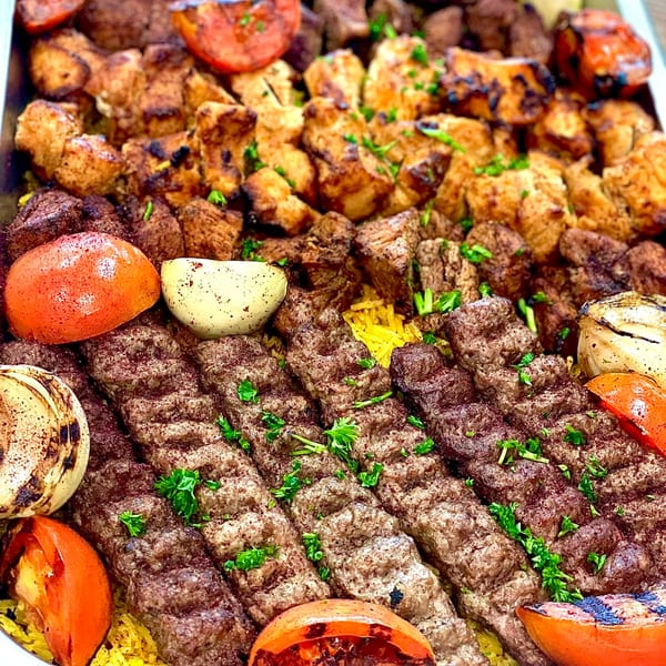 A large platter of grilled chicken, beef kebabs, and kofta, with roasted tomatoes and onions.